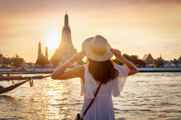 A woman enjoys the sunset view to the famous Wat Arun temple in Bangkok