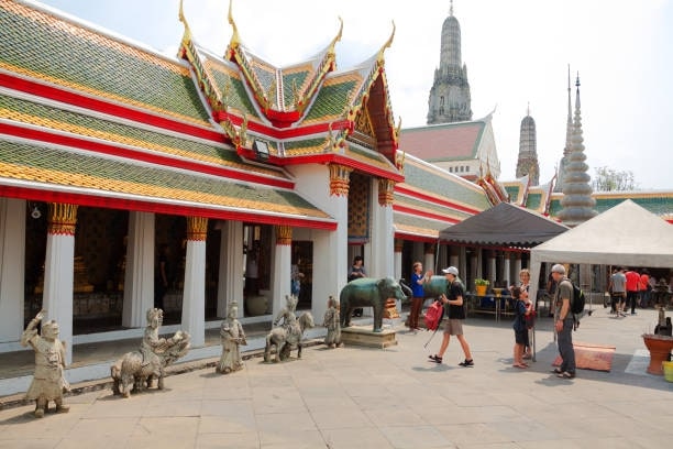 Several tourists are walking in courtyard with arcades with buddhas of Wat Arun in Bangkok