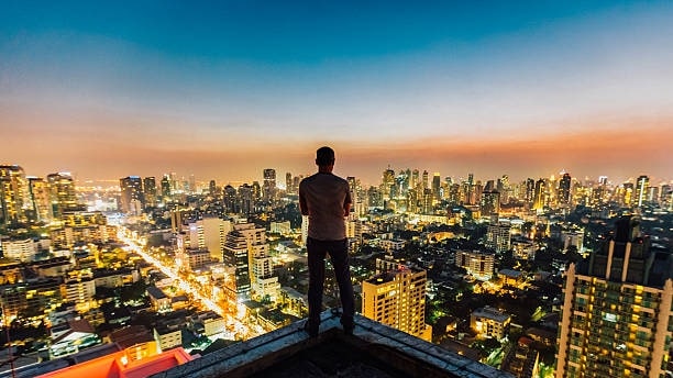 man on the edge of a building looking at the city lights